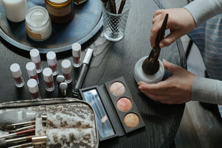 Personne appliquant de la poudre avec un pinceau de maquillage sur une table remplie de produits cosmétiques.